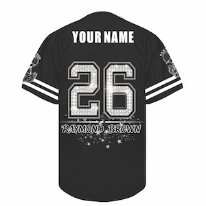 May include: A black short-sleeve jersey featuring the text YOUR NAME at the top, the number 26 in a silver diamond-like pattern in the center, and the name RAYMOND BROWN printed below with a decorative star graphic at the bottom hem.