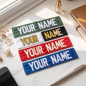 Può includere: Cinque toppe rettangolari in tessuto con testo ricamato. Una toppa verde, una bianca, una nera, una rossa e una blu, ognuna con le parole YOUR NAME in lettere maiuscole in grassetto e in stile blocco con fili di colori contrastanti.