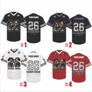 May include: Four short-sleeved sports jerseys in black, purple, white, and red. Each features the number 26, the text RAYMOND BROWN, and a graphic of two figures. The back displays the text YOUR NAME above the number 26 and RAYMOND BROWN.