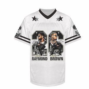 May include: A white V-neck jersey with black trim on the sleeves and collar. The front features two large graphic panels with illustrations of Usher Raymond and Chris Brown, each with the text "RAYMOND" and "BROWN" printed below the images.