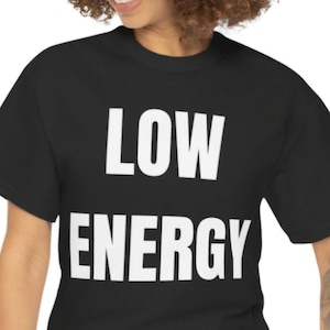 May include: Black t-shirt with the words "LOW ENERGY" printed in large, white, bold letters. The text is centered on the front of the shirt. The shirt has short sleeves and a crew neck.