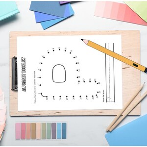 May include: A wooden clipboard holds a white page from an alphabet booklet with the letter "A" as a connect-the-dots activity. A yellow pencil rests on the page. Other stationery items, including colored paper swatches, are scattered around.