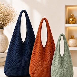 Può includere: Tre borse a sacco realizzate in tessuto lavorato a maglia testurizzato. Le borse sono disposte per dimensione da sinistra a destra: una grande borsa blu navy scuro, una media color arancio bruciato e una piccola verde salvia con manico.