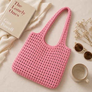 May include: A bright pink crochet tote bag featuring an open square grid pattern and two integrated shoulder straps. The bag is constructed with a consistent yarn texture and a rectangular shape, showcasing a vibrant solid color throughout the design.