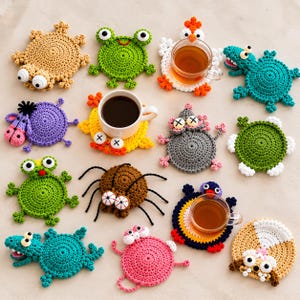 Könnte beinhalten: Eine Sammlung von vierzehn runden Häkeluntersetzern mit verschiedenen Tiermotiven wie Frosch, Spinne, Huhn, Schildkröte und anderen Kreaturen mit Wackelaugen, von denen einige klare Glastassen mit Kaffee oder Tee halten.