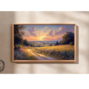 Pode incluir: Pintura de paisagem emoldurada que retrata um pôr do sol sobre uma cena rural. Um caminho de terra serpenteia por um campo de flores silvestres, levando ao horizonte. O céu é preenchido com nuvens laranja e roxas, e a pintura é emoldurada em madeira clara.