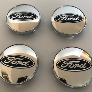May include: Four chrome hubcaps with the Ford logo in black script on a black oval. The hubcaps are circular with a shiny, reflective surface.