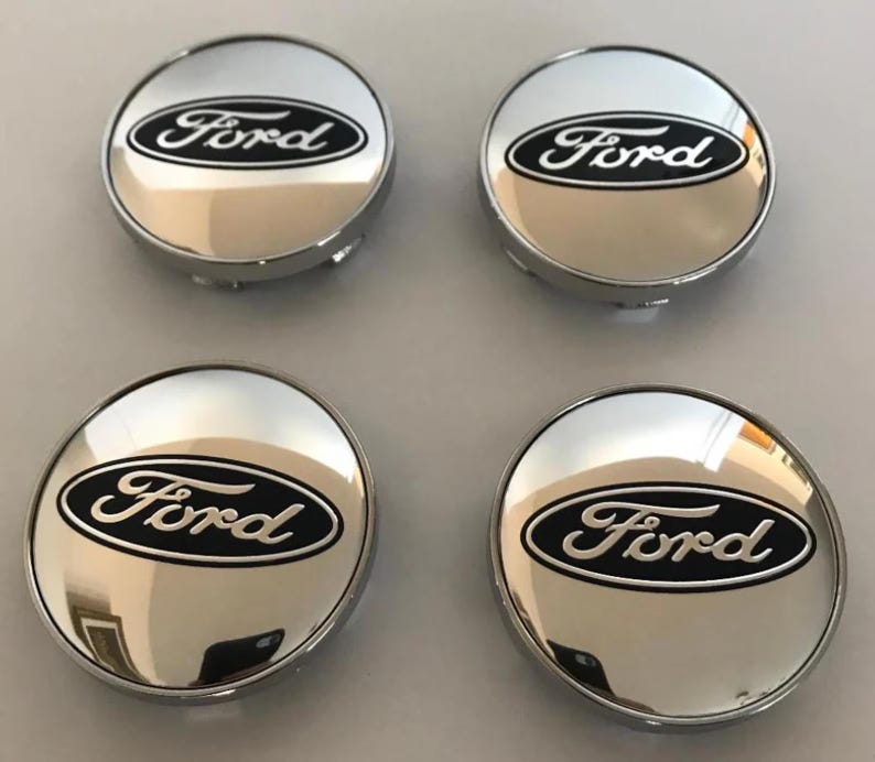 May include: Four chrome hubcaps with the Ford logo in black script on a black oval. The hubcaps are circular with a shiny, reflective surface.