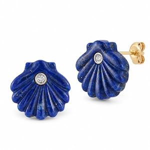 May include: A pair of stud earrings shaped like scallop shells carved from deep blue lapis lazuli with gold flecks. Each earring features a small, round, clear gemstone set in a silver-toned bezel at the center, attached to a gold-toned post backing.
