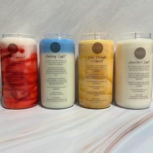 May include: Four cylindrical glass candles with labels. The first is red and white, labeled Love & Support. The second is blue and white, labeled Healing Light. The third is yellow and white, labeled Solar Strength & Support. The fourth is white, labeled Ancestors Light.