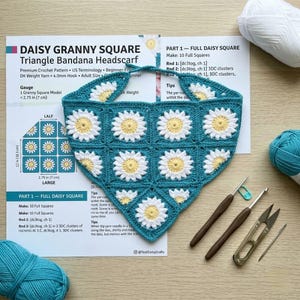 May include: A handmade teal granny square triangle bandana headscarf with white and yellow daisy flower designs. The crochet pattern includes instructions and is accompanied by crochet hooks, scissors, and yarn.
