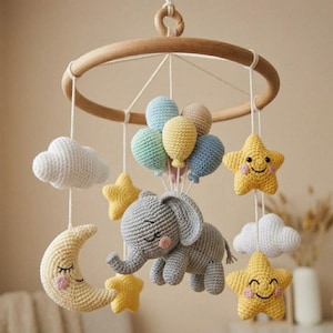 Könnte beinhalten: Handgefertigtes Baby-Mobile mit einem gehäkelten grauen Elefanten, der bunte Luftballons hält. Das Mobile umfasst gelbe, lächelnde Sterne, weiße Wolken und einen Mond, die alle an einem Holzring aufgehängt sind.