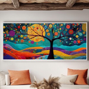 Könnte beinhalten: Ein gerahmter Kunstdruck mit einem farbenfrohen Baum mit einer großen gelben Sonne. Der Baum hat einen schwarzen Stamm und Äste mit leuchtenden Blättern und Früchten. Der Hintergrund zeigt sanfte Hügel in Blau-, Orange- und Lilatönen. Das Kunstwerk wird über einem weißen Sofa ausgestellt.