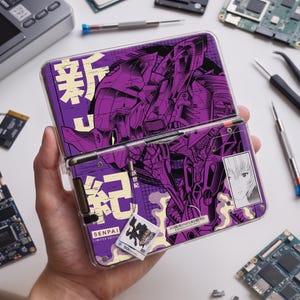 May include: A purple handheld gaming console featuring a graphic of a mechanical robot, Japanese characters, and a small portrait of a person. The device includes a small white tag labeled SENPAI LIMITED EDITION and a clear protective case.