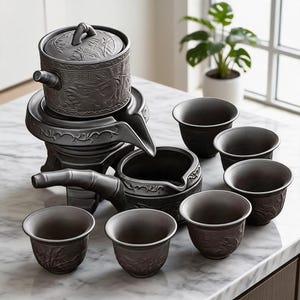 May include: A dark grey ceramic tea set featuring a teapot, server, and six cups. The teapot has a lid and is decorated with relief carvings. The server has a bamboo-shaped handle. The cups have a slightly flared shape and are also decorated with relief carvings.