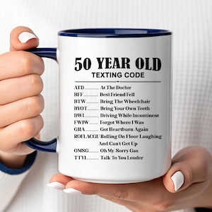 May include: White ceramic mug with a navy blue interior and handle, featuring the text "50 YEAR OLD TEXTING CODE" in black. The mug lists humorous acronyms like "BFF - Best Friend Fell" and "DWI - Driving While Incontinent".