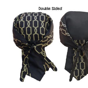 Pode incluir: Bandana de dupla face preta e dourada com design de corrente. A bandana é amarrada em um nó na parte de trás do pescoço.