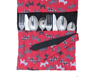 May include: A red and black fabric cutlery roll with a repeating pattern of white, black, and checkered dog silhouettes. The roll contains stainless steel forks, knives, and spoons. A black strap secures the roll.