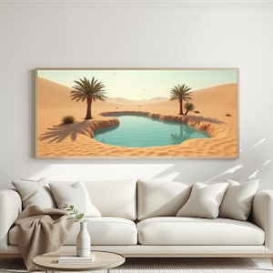 Puede incluir: Una impresión enmarcada de un paisaje de oasis desértico con una piscina turquesa y dunas de arena. Las palmeras proyectan sombras bajo un cielo brillante. La obra de arte se muestra sobre un sofá blanco.