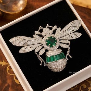 Broche de abeja chapado en oro blanco de 14 quilates con esmeralda sintética de 2 quilates de talla redonda.