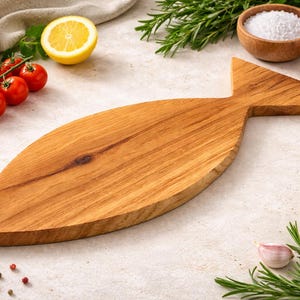 May include: A wooden fish-shaped cutting board with a light brown finish. The board is surrounded by fresh ingredients, including tomatoes, lemon, garlic, rosemary, and spices. The board is approximately 20 inches long.