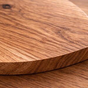 May include: Close-up of a wooden cutting board with a curved edge. The board is made of light brown wood with visible grain patterns. The surface is smooth and appears to be well-finished, suggesting a quality kitchen item.