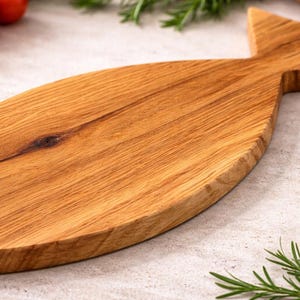 May include: A wooden cutting board in the shape of a fish. The board is made of light brown wood and has a natural wood grain pattern. The board is surrounded by fresh tomatoes, herbs, and spices.