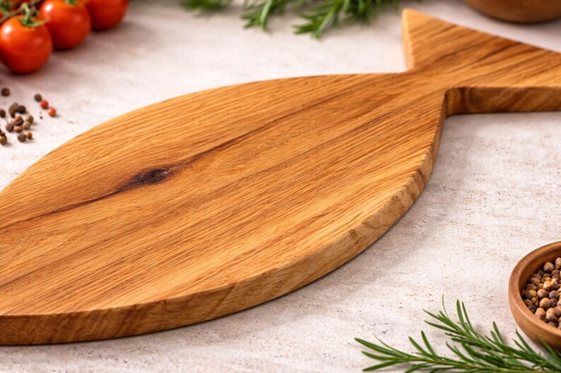 May include: A wooden cutting board in the shape of a fish. The board is made of light brown wood and has a natural wood grain pattern. The board is surrounded by fresh tomatoes, herbs, and spices.