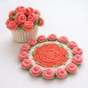 May include: A handmade crochet set featuring a floral theme. The set includes a cream-colored basket filled with coral-colored roses and a matching round coaster. The coaster has a coral center, surrounded by cream, green, and coral rose accents.