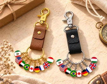 May include: Two keychains featuring leather straps, one brown with gold-tone hardware and one black with silver-tone hardware. Each keychain has a circular ring attached to multiple small, round metal charms displaying various national flags.