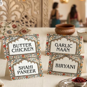 May include: Four table cards with Indian dish names: Butter Chicken, Garlic Naan, Shahi Paneer, and Biryani. The cards feature a floral border design and a white background. The Canva logo is in the upper left corner.