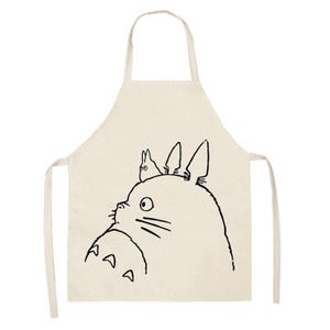 Puede incluir: Delantal beige con un dibujo lineal negro de un personaje de Totoro. El delantal tiene un lazo para el cuello y lazos en la cintura. El dise&ntilde;o de Totoro incluye la cara del personaje y una criatura m&aacute;s peque&ntilde;a en su cabeza. Un divertido accesorio de cocina.