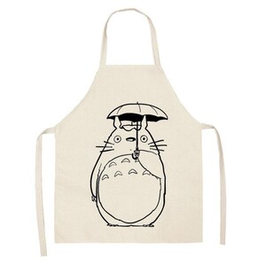 Puede incluir: Delantal beige con una ilustraci&oacute;n en blanco y negro de un personaje de dibujos animados sosteniendo un paraguas. El delantal tiene un lazo para el cuello y lazos en la cintura, adecuado para cocinar o manualidades.