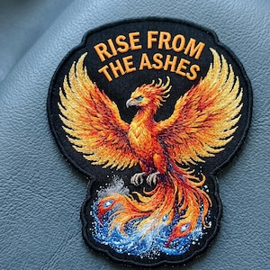 May include: Embroidered patch featuring a phoenix rising from flames. The patch has a black background with the words "RISE FROM THE ASHES" in orange. The phoenix is depicted in shades of orange, yellow, and red, with blue accents.