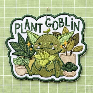May include: An embroidered patch featuring a green goblin character holding a small potted plant, surrounded by various potted houseplants. The text "PLANT GOBLIN" is stitched in dark green above the character, with yellow star accents.