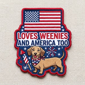 May include: A rectangular embroidered patch featuring the American flag at the top, the text LOVES WEENIES AND AMERICA TOO in red and blue, and a tan dachshund wearing a star-patterned bandana next to a firework rocket on a blue background.
