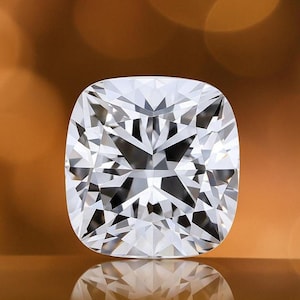Op de afbeelding: Een kussenvormige diamant met een briljant, facetrijk ontwerp. De heldere edelsteen reflecteert licht, waardoor een sprankelend effect ontstaat. De diamant is geplaatst tegen een warme, vage achtergrond.