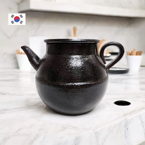 May include: A dark brown ceramic teapot with a spout and handle. The teapot has a rounded body and a textured surface. The background is a kitchen countertop.