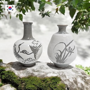 May include: A set of three ceramic mugs with a speckled, matte finish. The mugs are in shades of cream, light gray, and dark gray. Each mug has a simple, minimalist design and a rounded handle.