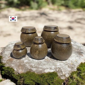 May include: A set of three ceramic mugs with a speckled, matte finish. The mugs are in shades of cream, light gray, and dark gray. Each mug has a simple, minimalist design, perfect for coffee or tea.