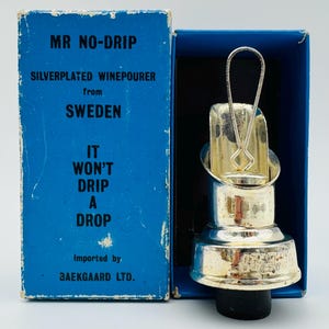 May include: A silver-plated wine pourer with a black rubber stopper, presented in a blue box. The box reads "MR NO-DRIP" and "SILVERPLATED WINEPOURER from SWEDEN". The pourer has a loop handle and is designed to prevent drips.