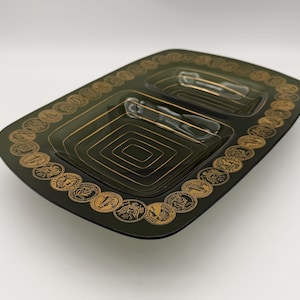 May include: Dark green rectangular serving dish with two compartments and gold accents. The dish has a border of gold coin-like designs and gold geometric patterns inside the compartments. Includes two serving utensils.
