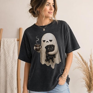 Pode incluir: Uma t-shirt cinzento-carvão de manga curta com um gráfico de um fantasma branco a segurar uma caneca castanha com o texto MEH e um pug preto. A camisola tem um decote redondo e um corte descontraído em tecido com aspeto vintage.