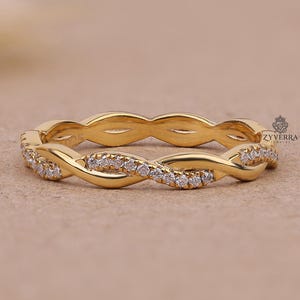 May include: A gold ring featuring a twisted, interwoven band design. One half of the band is smooth, polished gold, while the other half is encrusted with small, clear, sparkling stones. The ring includes a small logo mark reading Zyverra.