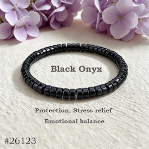 May include: A circular bracelet composed of small, glossy black onyx disc beads. The text Black Onyx, Protection, Stress relief, Emotional balance, and #26123 is printed in the centre and bottom of the image, surrounded by light purple flowers.
