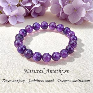 Peut inclure: Un bracelet circulaire composé de perles d'améthyste violettes polies. Le texte sous le bracelet indique : Natural Amethyst. Eases anxiety - Stabilizes mood - Deepens meditation. Les perles sont disposées en une boucle à un seul rang.