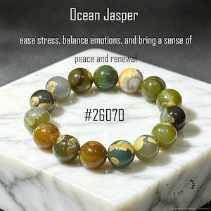 Op de afbeelding: Ocean Jasper kralenarmband. De armband heeft ronde kralen in tinten groen, bruin, geel en grijs. De tekst op de afbeelding luidt "Ocean Jasper" en "ease stress, balance emotions, and bring a sense of peace and renewal". De productcode is #26070.