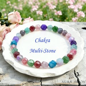 May include: A multi-colored Chakra stone bracelet with faceted beads, displayed on a white plate. The bracelet features a variety of colors, including red, green, blue, purple, and pink. The text "Chakra Multi-Stone" is written in blue.