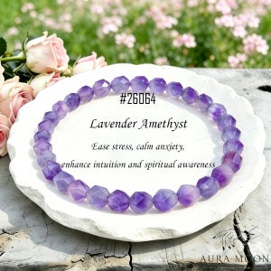 Op de afbeelding: Een armband van lavendel amethist kralen met facetten. De armband ligt op een wit bord. De tekst luidt: "#26064 Lavendel Amethist Verminder stress, kalmeer angst, verbeter intuïtie en spiritueel bewustzijn."