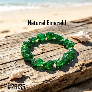 May include: A bracelet composed of raw, deep green emerald stones strung together with small clear spacer beads. The text Natural Emerald and the number #26135 are visible in the image. The bracelet features irregular, faceted gemstone pieces.